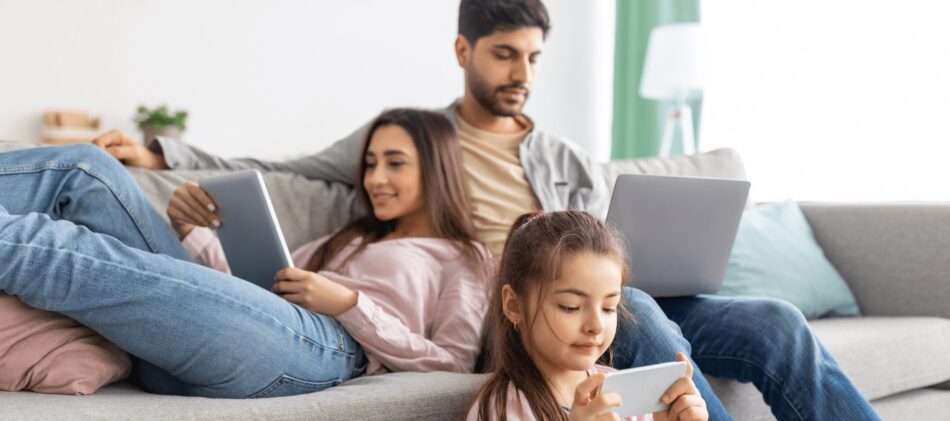 Young family sitting in their living room looking at tabs and laptops