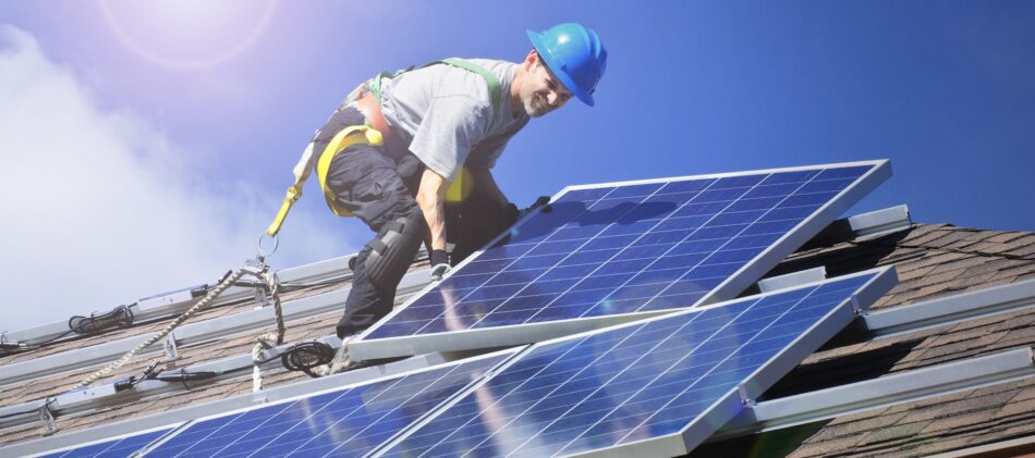 Roof worker harnessed in and putting down solar panels
