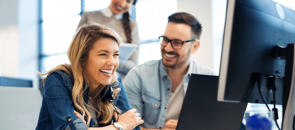 Two coworkers in an office looking at computer and laughing together