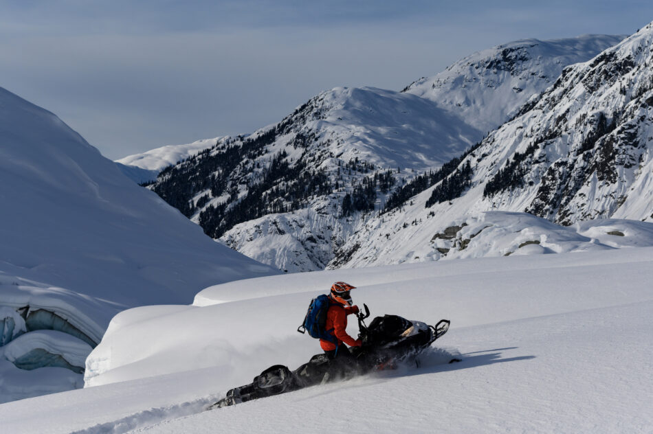 Backcountry snowmobiler rides across glacier through fresh powder snow, Whistler
