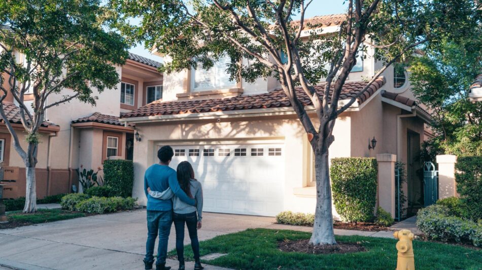 Back view of young couple looking at two storey home from driveway and hugging