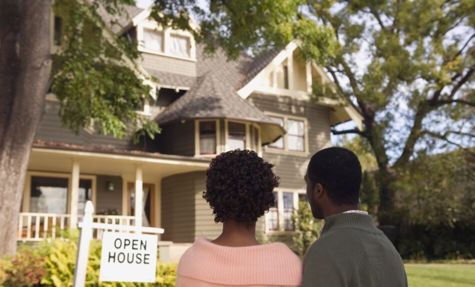 Couple looking at the exterior of a house with Open House sign out front