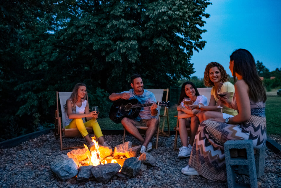Summer vacation, holidays and people concept. Singing and playing guitar by the campfire.