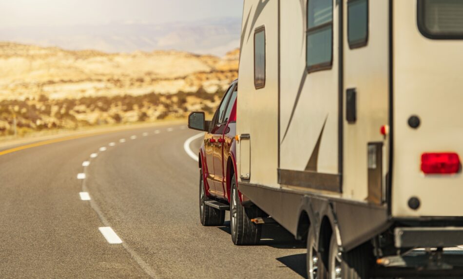 Back view of a truck pulling an RV while driving down winding road with dry desert-like surroundings